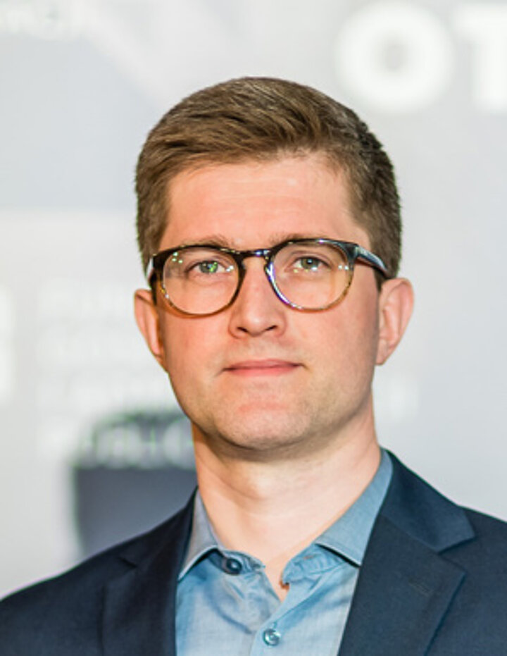 Portrait photo of a man in a blue suit and black glasses.